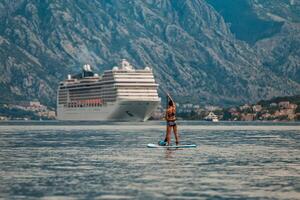 solo paddle boarder in front of a towering cruise ship with a stunning mountainous backdrop photo