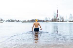 Young man taking an ice bath Swimming in a lake during winter Healthy cold swim photo
