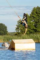 Young man wakeboarding on a lake, making raley, frontroll and jumping the kickers and sliders Wakeboard photo