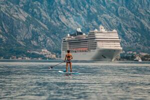 solo paddle boarder in front of a towering cruise ship with a stunning mountainous backdrop photo