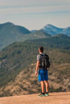 hiker with backpack standing on mountain peak overlooking a stunning mountain range photo