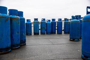 array of used blue propane gas cylinders lined up on concrete floor, essential supplies for industrial welding and heating tasks photo