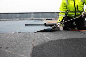 professional roofer applying bitumen roll on flat roof with a gas burner at a modern construction site photo