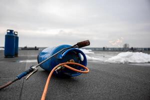 gas torch tool lying on new roofing surface with propane tank and hose, essential equipment for construction workers for melting and sealing tar on flat roof photo