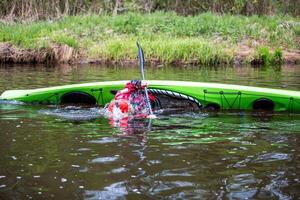 adventurous kayaker in a bright green kayak practicing the eskimo roll technique in a calm river surrounded by lush vegetation during an overcast day photo