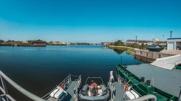View from a Military Patrol Boat Navigating River with Industrial Port Horizon and Blue Sky photo