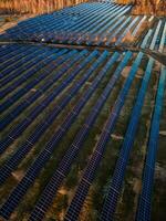 Aerial view of a large solar farm at sunset with rows of photovoltaic panels amidst a natural landscape, showcasing renewable energy photo