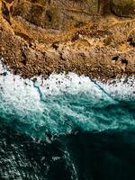 Aerial view of rocky beach with waves and clear ocean water. Drone top view photo