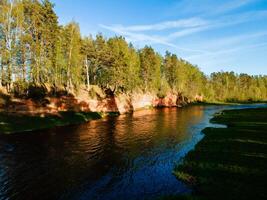 panoramic view of the red cliffs along the riverbank in latvia with lush forest and vibrant water photo
