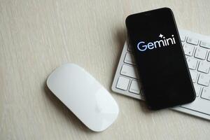KYIV, UKRAINE - MARCH 17, 2024 Gemini logo on iPhone display screen with apple keyboard and mouse on table photo