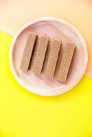 Chocolate waffles on wooden plate isolated on orange and yellow background. Crispy snack dessert. Food Photography Concept photo