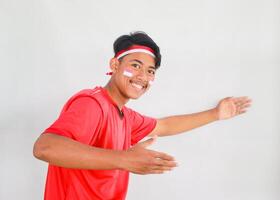 handsome young man in a red shirt and headband pointing to the copy space beside him, isolated white background, celebrating indonesia's independence day. Indonesia Independence Day concept. photo