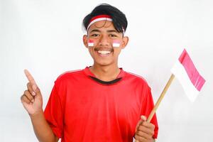 handsome young man in a red shirt and headband pointing to the copy space beside him, isolated white background, celebrating indonesia's independence day. Indonesia Independence Day concept. photo
