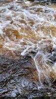 abstract background with foam waves crashing against rocks and stones. vertical nature photography. mountain river and forest photo