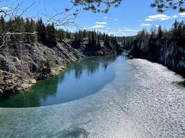 stone quarry lake covered with thin ice. nature of Europe with rocks, green pine forest and pond. horizontal photograph of landscape taken on sunny day photo