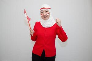 Woman in white hijab wearing red sweater. celebrating Indonesia's independence day. holding a flag with a happy face. looking at the camera. isolation on white background. photo