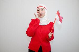 Woman in white hijab wearing red sweater. celebrating Indonesia's independence day. holding a flag with a happy face. looking at the camera. isolation on white background. photo