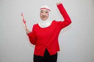 Woman in white hijab wearing red sweater. celebrating Indonesia's independence day. holding a flag with a happy face. looking at the camera. isolation on white background. photo
