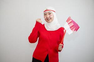 Woman in white hijab wearing red sweater. celebrating Indonesia's independence day. holding a flag with a happy face. looking at the camera. isolation on white background. photo