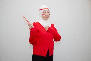 Woman in white hijab wearing red sweater. celebrating Indonesia's independence day. holding a flag and clenching his fists to his chest. isolation on white background. photo