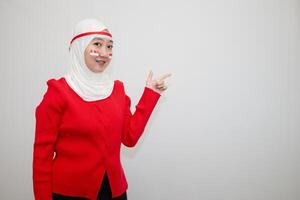 Woman in white hijab wearing red sweater. celebrating Indonesia's independence day. pointing to the side. isolation on white background. photo