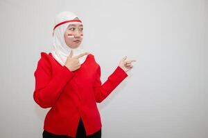 Woman in white hijab wearing red sweater. celebrating Indonesia's independence day. pointing to the side. isolation on white background. photo