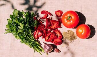 Appetizing dried and fresh tomatoes, various spices and herbs lie on the kitchen table, bright sunlight and shade photo