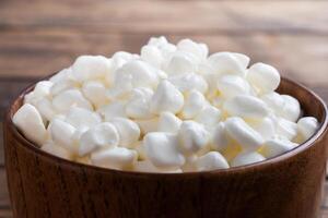 Fresh cottage cheese grain in a wooden bowl. Curd in granules with cream. Wooden rustic background. Copy space. photo