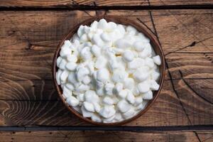 Fresh cottage cheese grain in a wooden bowl. Curd in granules with cream. Wooden rustic background. Copy space. photo