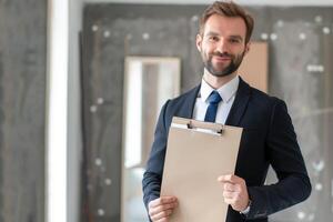 handsome real estate agent holds a folder in hands and shows an empty apartment, empty space for text photo