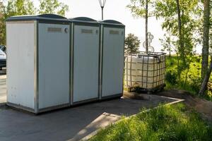 Three white portable toilets stand on a paved area in a park setting photo
