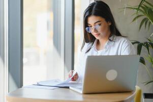 Beautiful Young Freelancer Woman Using Laptop Computer Sitting At Cafe Table. Happy Smiling Girl Working Online Or Studying And Learning While Using Notebook. Freelance Work, Business People Concept. photo