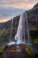 Tourist near the Majestic Seljalandsfoss Waterfall at Sunset, One of Icelands Most Iconic and Popular Tourist Attractions photo