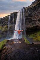 Tourist near the Majestic Seljalandsfoss Waterfall at Sunset, One of Icelands Most Iconic and Popular Tourist Attractions photo