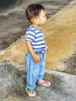 A boy in a blue striped shirt and jeans standing with a candy bar in his mouth. photo