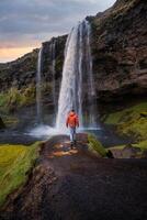 Tourist near the Majestic Seljalandsfoss Waterfall at Sunset, One of Icelands Most Iconic and Popular Tourist Attractions photo
