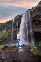 Tourist near the Majestic Seljalandsfoss Waterfall at Sunset, One of Icelands Most Iconic and Popular Tourist Attractions photo
