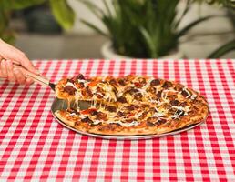 Woman hand takes a slice of pizza with spatula on table. photo