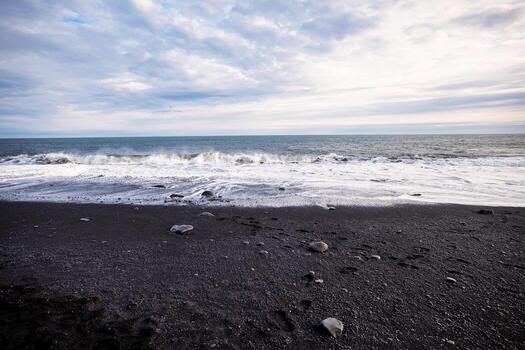 Waves crashing on the black sand shores of Reynisfjara beach in Iceland with a cloudy sky above photo