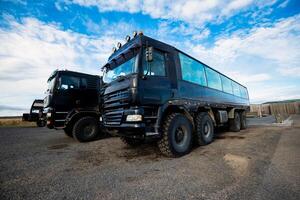Large off-road trucks parked on a gravel lot under a blue sky in Iceland. photo
