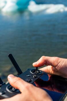 Hands operating a drone controller with a glacial lagoon in the background, Iceland photo