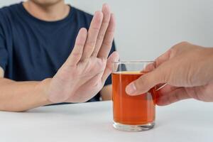 man refuses say no and avoid to drink an alcohol whiskey , stopping hand sign male, alcoholism treatment, alcohol addiction, quit booze, Stop Drinking Alcohol. Refuse Glass liquor, unhealthy, reject photo