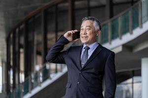 Senior business asian man is talking to mobile phone in the modern office for professional disscussion photo