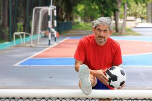 Senior Asian man in retirement age playing soccer football at outdoor court for healthy and fun activity to exercise and workout against aging illness photo