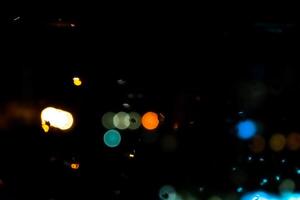 Mesmerizing urban bokeh through raindrops on window glass creating a cozy atmosphere. The glitter of bokeh city lights through the window. photo