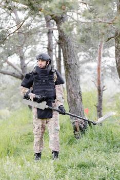 A man in a military uniform and bulletproof vest works in the forest with a metal detector. A minesweeper performs work on demining the territory photo
