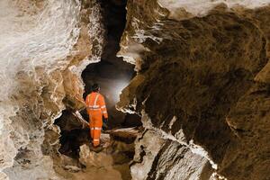 Man walking and exploring dark cave with light headlamp underground. Mysterious deep dark, explorer discovering mystery moody tunnel looking on rock wall inside. photo