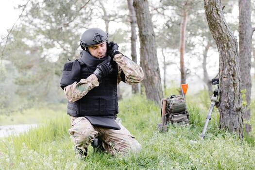 A man in a military uniform and a bulletproof vest works in the forest to demine the territory. A man puts on a protective helmet before starting work photo
