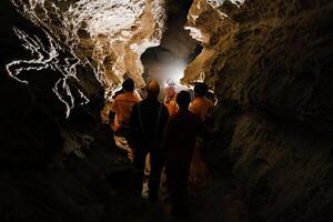 Five men, strong physique, explore the cave. Men dressed in special clothes to pass through the cave and stopped, looking at the map photo