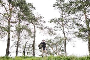 Young soldier in uniforms and tactical vest works in the forest and prepares for action at a temporary forest base. A man does in the work of demining the territory photo